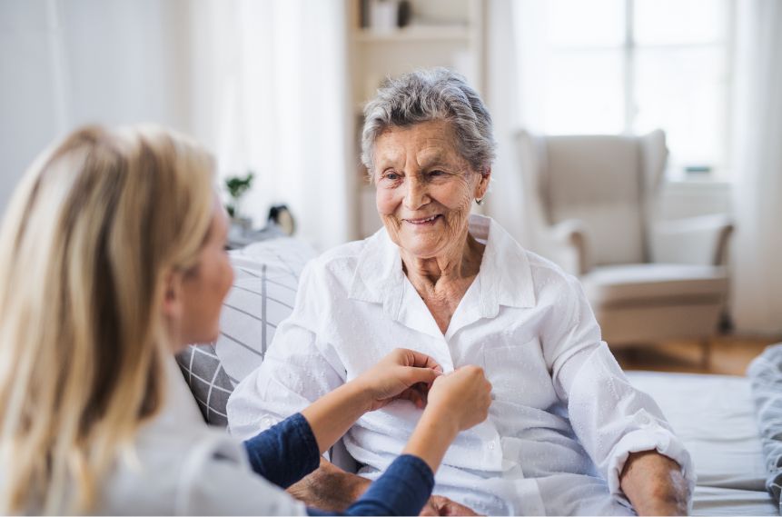 A woman helping an older woman button her shirt