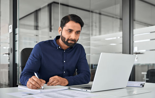 A man looking at a computer and writing something in a notebook